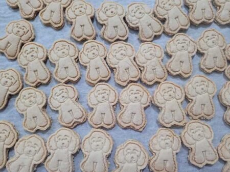 Baked chicken pet biscuits shaped like dogs, arranged on a baking tray.