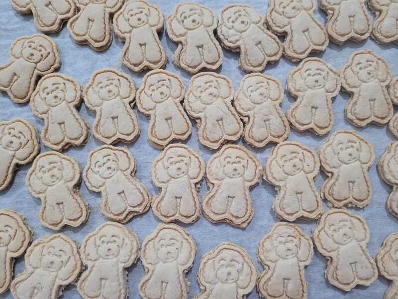 Baked chicken pet biscuits shaped like dogs, arranged on a baking tray.