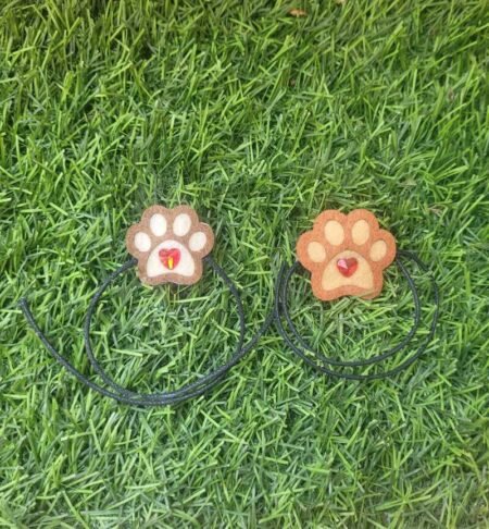 Two handmade paw-shaped Raksha Bandhan rakhis with heart details displayed on green grass.