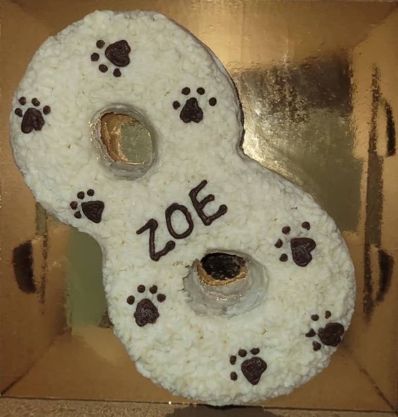 Number-shaped banana pet cake with white frosting, brown paw-print decorations and “ZOE” lettering.