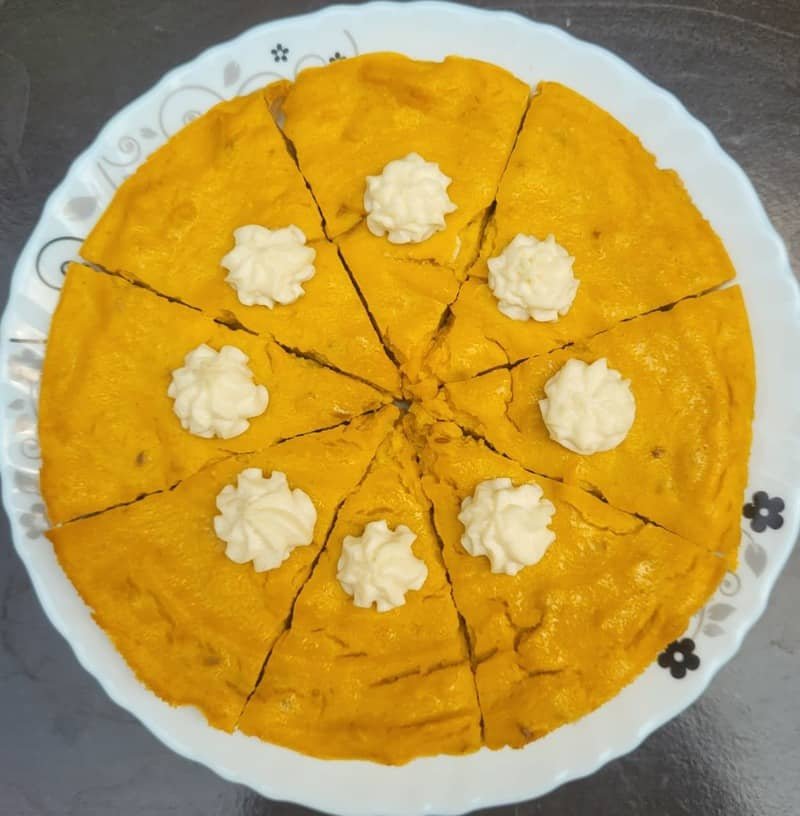 Pet-friendly pumpkin pie cut into slices and topped with white piped decorations on a serving plate.