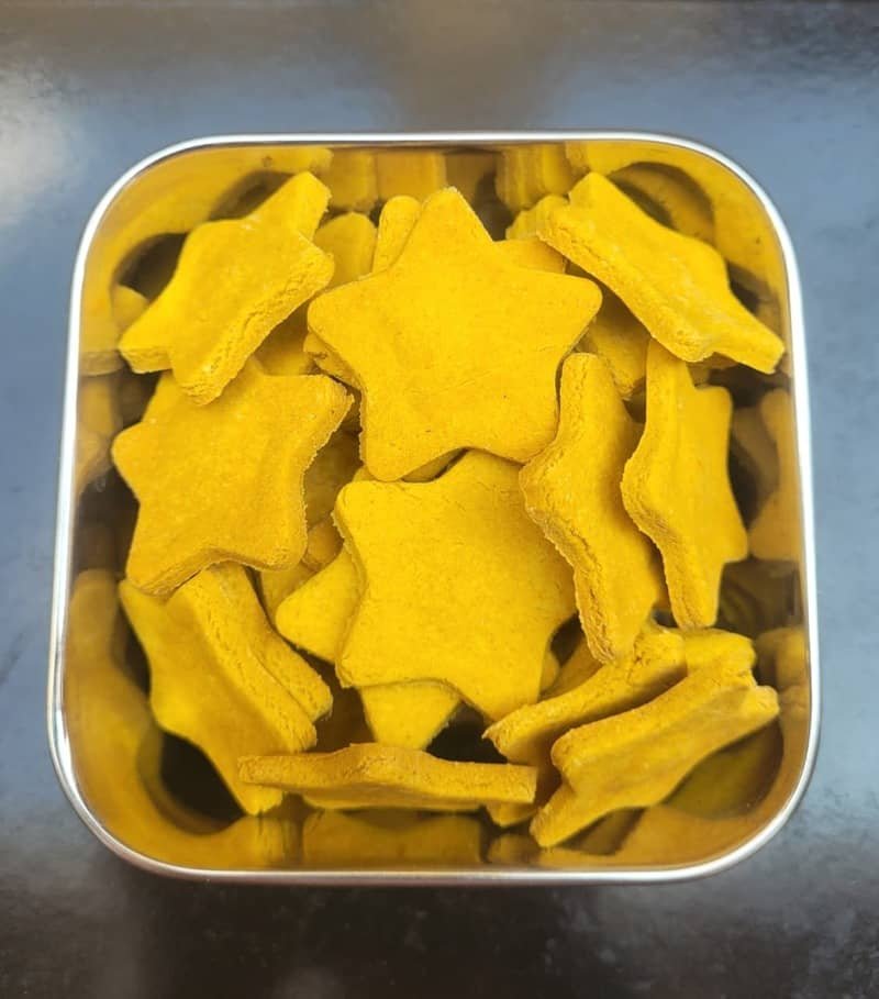 Golden-yellow star-shaped carrot biscuits for pets in a metal tin.